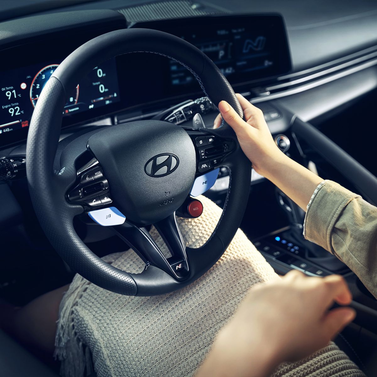 A learner's hands resting on a car steering wheel with the other hand on the gear lever