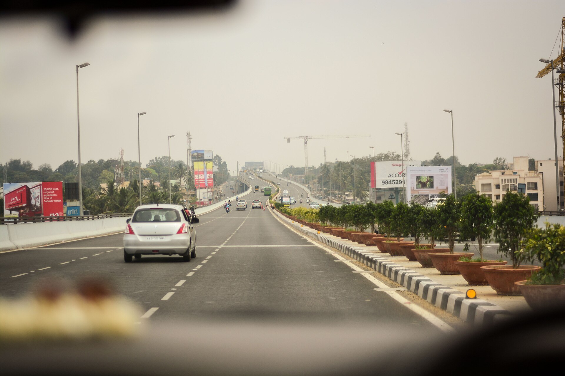 Driver's view of a Bengaluru arterial road with cars and two-wheelers ahead in daytime traffic