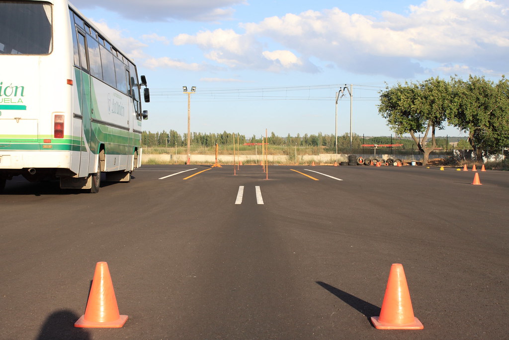 A driving school practice track marked with lanes and orange cones, with a training bus parked alongside