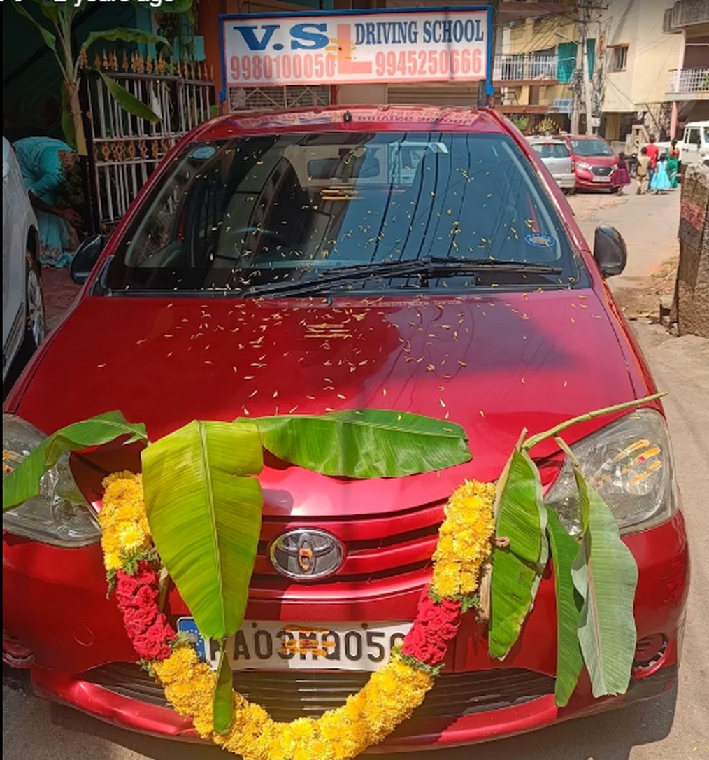VS Motor's red Toyota Etios training car with the V.S Driving School roof board, garlanded outside the GM Palya office